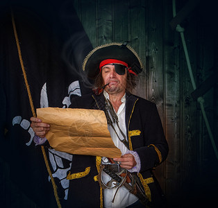 喜乐满堂成年海盗船长穿着传统服装手持在喜乐罗杰的背景下看一宝藏