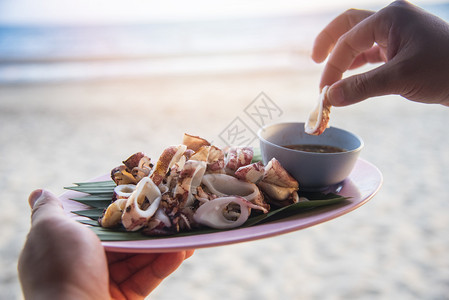 海滩背景上的灰状鱿鱼盘子里的鱿鱼切片手边有泰海鲜酱图片