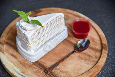 煎饼切片和草莓酱放在木板勺子上的草莓酱和黑暗背景蛋糕彩虹和奶油图片
