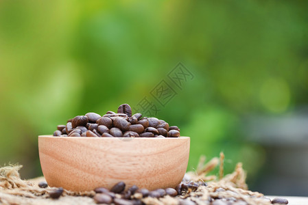 在木碗上烤煮咖啡豆和在木碗袋上烤咖啡豆在自然绿色背景上缝制咖啡豆图片