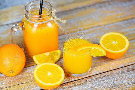 玻璃罐中的橙汁和木制桌上的新鲜橙子水果片图片