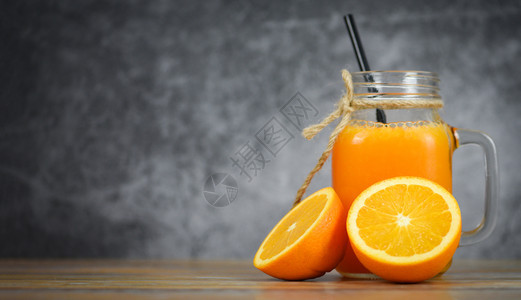 玻璃罐中的橙子汁和木制桌上的新鲜橙子水果片图片