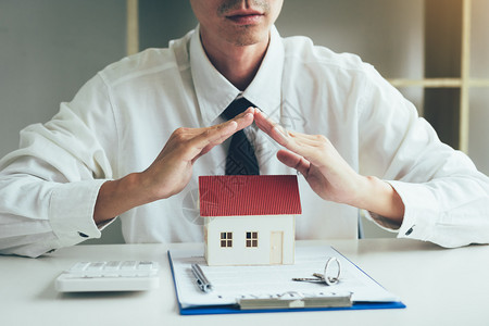 手盖或保护微型模范住房配有关于保险概念的键文件和合同图片