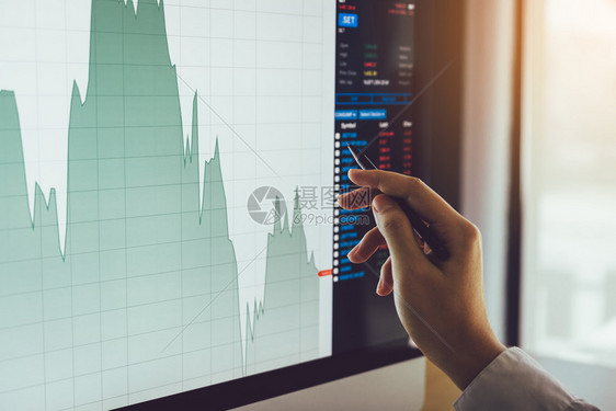 靠近商人的手指向股票市场图和计算机屏幕分析图片
