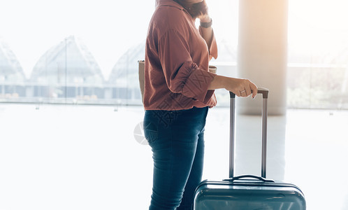 年轻的女子站在机场拿着手提箱准备登机图片