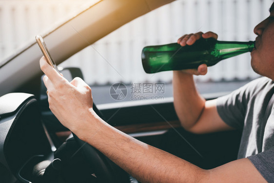 亚洲男子在车里喝酒开时使用手机图片