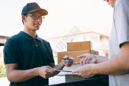 年轻的幼送货工作人员手持笔和向在前屋接收包裹的客户提交文件图片