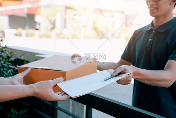 年轻的亚洲男子在向持有签名文件的妇女送纸箱时微笑图片