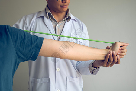 亚洲男理疗师的生治疗师在诊所工作帮助保护有病人在做伸展手术的病人在诊疗室用一个灵活的锻炼带进行伸展图片