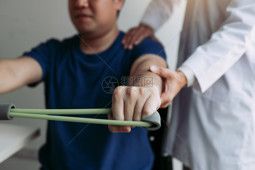 亚洲男理疗师血统与在诊疗室用灵活锻炼带进行伸展的病人一起工作图片
