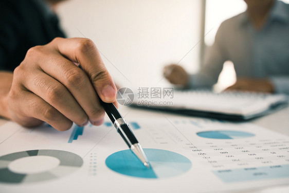 一名商人拿着笔指向财务报表或公司利润图并在办公室桌上分析图片