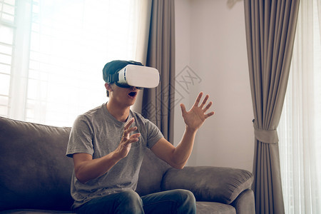 年轻的亚洲男子在客厅戴虚拟现实眼镜以欣赏虚拟现实图片