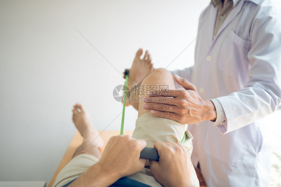 自信的理疗师帮助病人使用抗药带在诊疗室伸展腿部图片