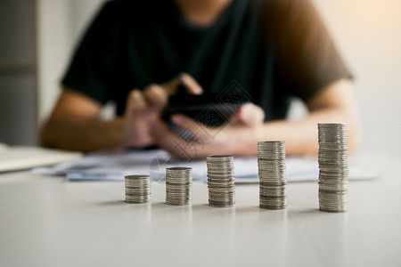 亚洲男子在计算家庭成本或未来投资的金而硬币则以储蓄的理念来安排图片
