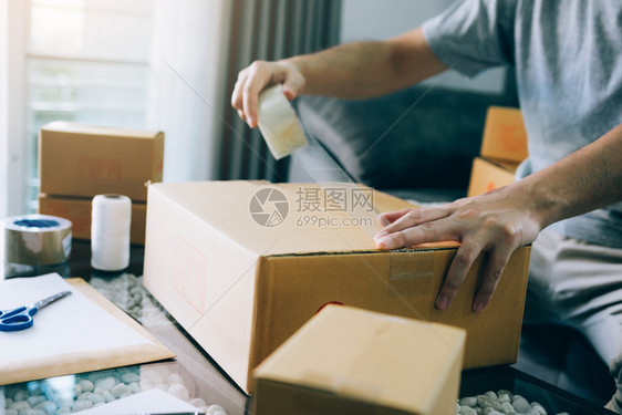 亚洲企业家青少年正在使用录像带通过包装产品寄给顾客密封盒子图片