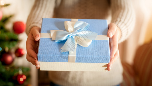 年轻女站在圣诞树上用丝带弓给蓝装礼物的盒照片冬季假日和庆祝活动的完美照片年轻女站在圣诞树上用丝带弓给蓝装礼物的盒照片冬季假日和庆图片