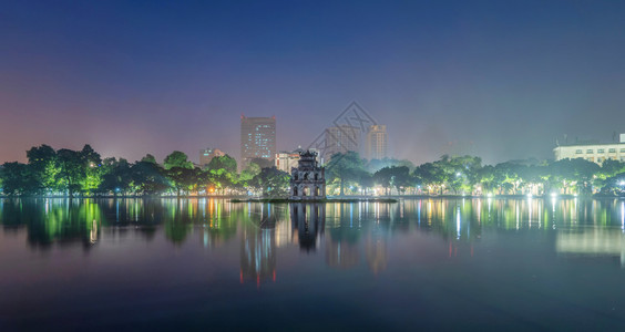 在河内市中心HoanKiem湖中央的海龟塔上有现代摩天大楼和反射塔晚上在越南城市背景背景图片