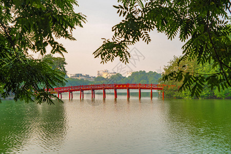 公园花中的红桥在河内市中心HoanKiem湖中间有树木和反射越南日落的城市景象背图片