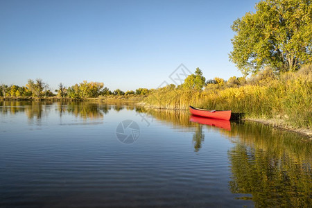 红色独木舟和一条划桨在平静的湖岸早期秋天风景图片