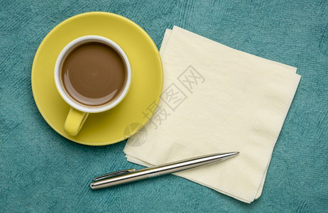 咖啡杯餐巾纸和笔板放在手工制作的绿树皮纸上图片