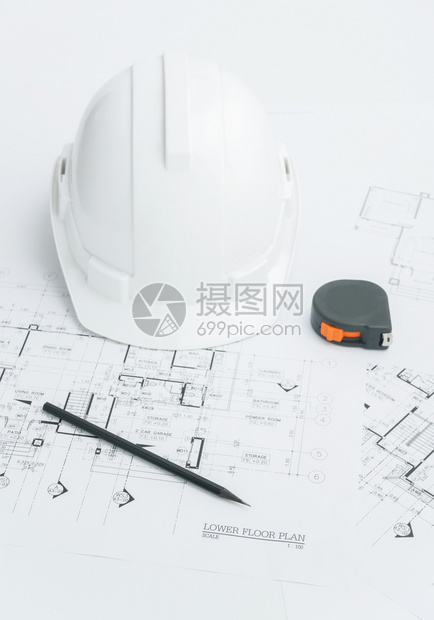 建筑师工作场所建筑蓝图上面有测量胶带安全头盔和桌面上的工具图片