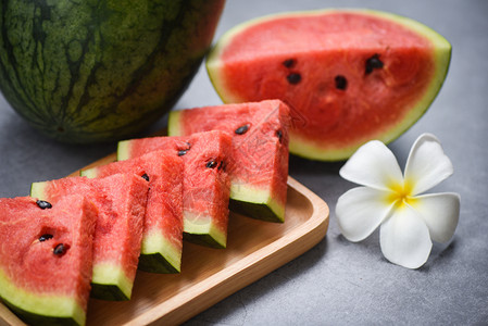 黑色背景的新鲜西瓜切片和白花木盘上的西瓜热带水果有选择的焦点图片