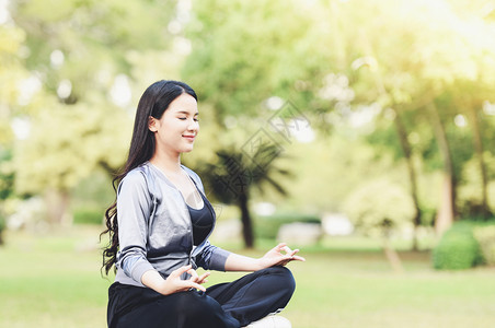 瑜伽女青年手在户外公园绿草地上做瑜伽和放松默思图片