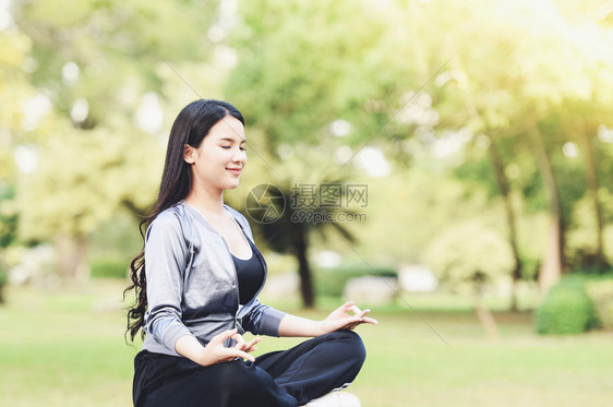 瑜伽女青年手在户外公园绿草地上做瑜伽和放松默思图片