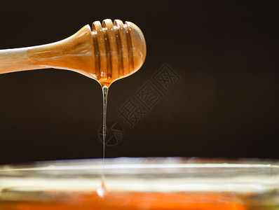 蜜蜂从罐子和黑暗背景的木制花蜜中滴黄糖有选择地聚焦图片