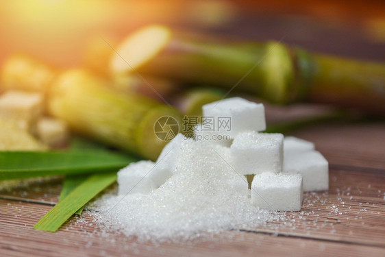 木制桌上的白糖立方和甘蔗以及阳光下的自然背景图片