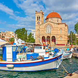 在希腊萨罗尼群岛Aegina镇阳光明媚的夏日与EkklilisiaIsodiaTheotokou教堂一起乘船和码头图片