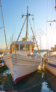 希腊萨罗尼群岛日落时在Aegina港的旧白渔船图片