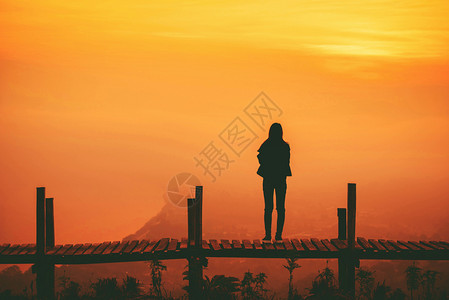 站在桥上的女人站在山的木桥上和黄的天空背景上女人背景