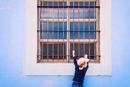 窗户小院男孩在蓝色的墙壁上爬到窗户的柱子上com背景