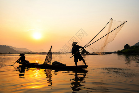 户外钓鱼在湄公河中使用木造船抛出净日落或的亚洲渔网具有山地背景生命的Silhouette渔船背景