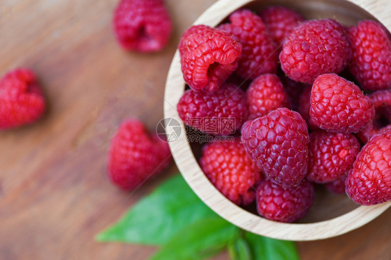 木碗中的新鲜树莓关闭红草莓果和绿叶顶视图图片
