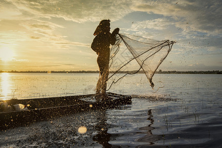 亚洲渔民利用木船净网捕捞在河中投下净日落或Silhouette渔民站在农村的船人上图片