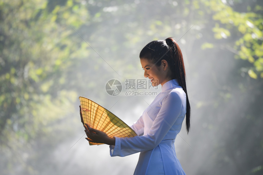 亚洲妇女维特南或中华风格的服装美丽年轻女孩外衣穿着传统服装的肖像在自然背景上手握着帽子编织叶图片