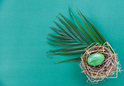 以绿底色棕榈叶为背景的篮子巢装饰复活节鸡蛋顶视图图片