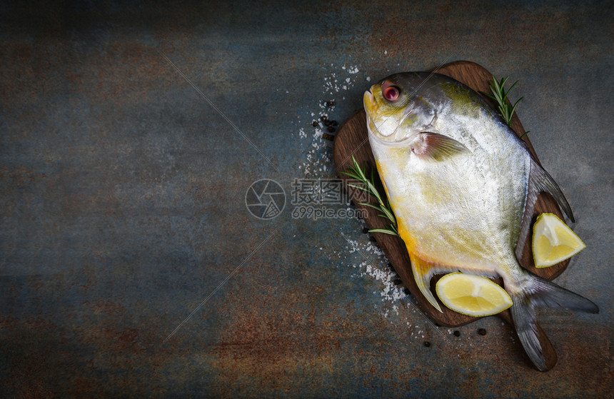 含有草药香料的新鲜乌黑鱼迷迭香和木制切板上的柠檬和黑底鱼原乌鱼图片