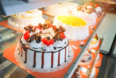 在商店面包糕饼甜巧克力牛奶和供销售的草莓水果蛋糕上展示的式玻璃中不同种类的蛋糕盘图片