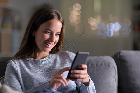 在家里晚上坐客厅沙发检查手机内容的快乐妇女图片