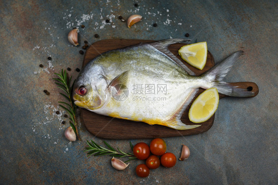 含有草药香料的新鲜乌黑鱼西红柿和木制切板上的柠檬以及黑板底鱼原乌鱼图片