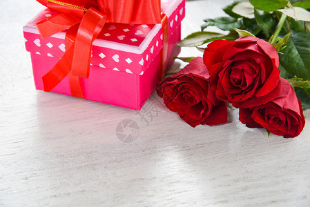 粉红礼物盒带丝弓红玫瑰花放在白色木背景复制空间上图片