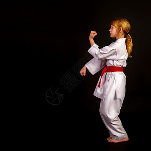 身穿运动和服的小女孩红腰带在黑暗背景下卡塔进行操练图片