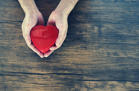 给爱人握着红心的情节捐赠帮助爱给温暖在木桌生锈背景的照顾概念图片