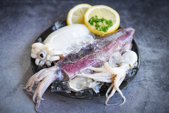 黑板底黑板上含有冰和沙拉香料的柠檬生鱿鱼新鲜乌贼章鱼或餐饮海鲜市场烹饪食品的甲头鱼图片