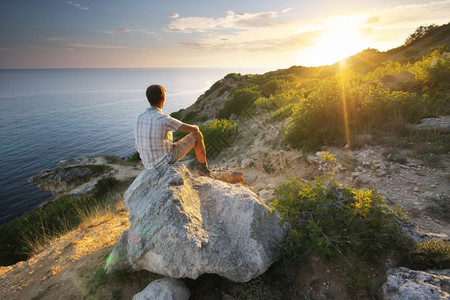 一个人坐在山上的岩石看着日出图片