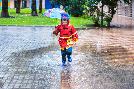 穿着红色雨衣的男孩伪装成雨伞喷洒在水坑里图片