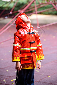 穿着红色消防员雨衣的有趣孩子在雨天公园玩耍图片
